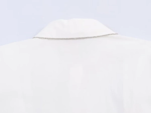 Close-up of a delicate silver chain necklace layered over a white poplin shirt collar