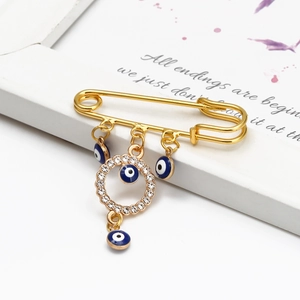 Detailed view of a gold safety pin brooch with blue evil eye beads and crystal charms