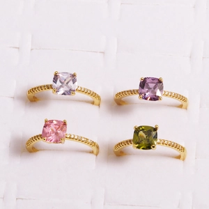 Close-up of four gold rings with square zircon stones in purple, pink, and olive green