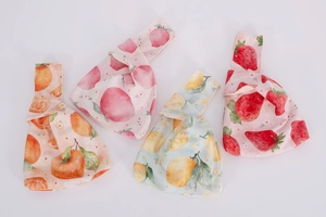 Detail of four velvet knot wrist bags with watercolor fruit prints on white background