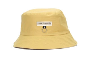 Detail of yellow cotton bucket hat with white text patch and metal ring accessory