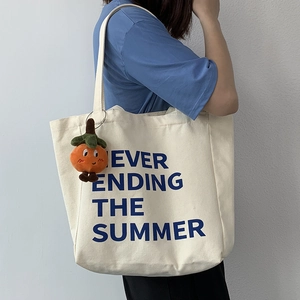Detail of a beige canvas tote bag with blue summer text and orange persimmon charm