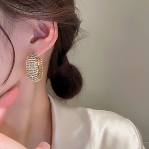 Primo piano di una modella che indossa ampi orecchini a C dorati con file di strass bianchi