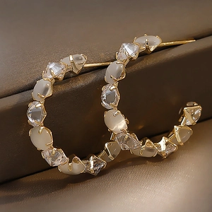 Macro shot of gold C-hoop earrings featuring white opal stones and clear square zircons