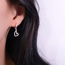 Detail of silver heart-shaped drop earrings with micro-set zircons on the model