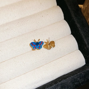 Macro shot of blue butterfly stud earrings with red crystals in a cream jewelry box