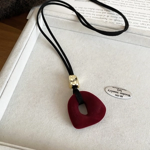 Macro shot of burgundy flocked resin pendant with gold metal clasp on black velvet cord