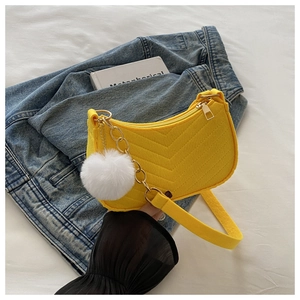 Bolso de fieltro amarillo con cadena metálica y pompón blanco sobre unos vaqueros
