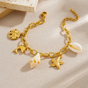 Gold-plated ocean charm bracelet with starfish, dolphin, and shell pendants on beige stone