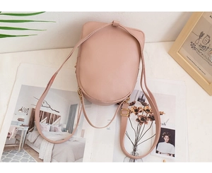 Rear view of a small pink quilted backpack displayed on an open magazine with green leaves