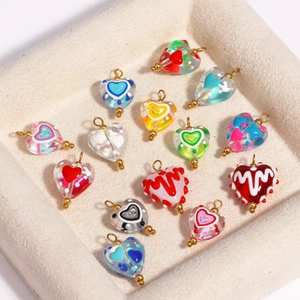Close-up of 13 colorful heart-shaped glass pendants with gold rings in a beige tray