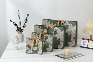 Detail of four green floral gift bags in different sizes with elegant gold ribbon handles