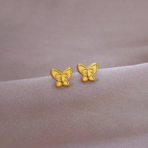 Macro view of gold butterfly stud earrings on silky fabric showing fine metal texture