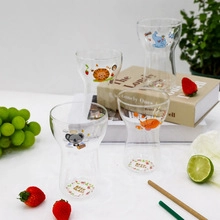 Detail of four clear glass cups with cartoon animal prints on a bright white table