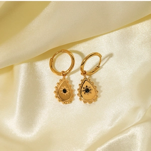 Detailed view of 18k gold plated drop earrings with black gemstones on beige silk fabric