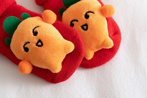 Close-up of baby Christmas socks with red knit texture and 3D plush carrot decoration