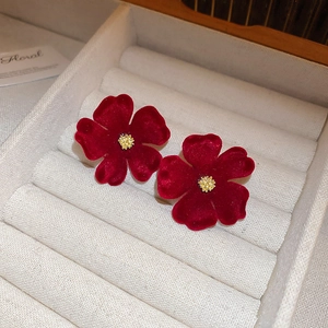 Dettaglio di orecchini a fiore in velluto rosso scuro con stame dorato in scatola