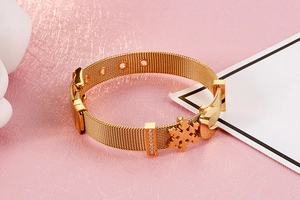 Dettaglio del bracciale in maglia d'acciaio dorata con ciondoli a luna e fiocco