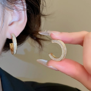 Close-up of gold C-shaped earrings with micro-paved zircons worn by a model