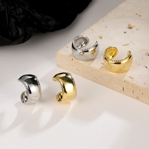Polished gold and silver wide-surface ear cuffs displayed on a marble base