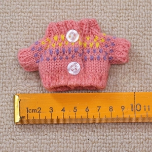 Macro shot of 9cm pink knitted doll sweater with yellow accents and white buttons