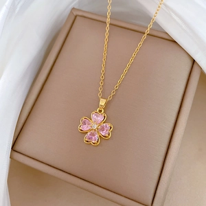 Macro detail of gold clover necklace with pink heart gems on a premium jewelry box