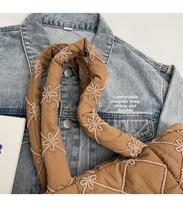 Detail of coffee brown quilted tote bag with floral stitching on denim jacket texture