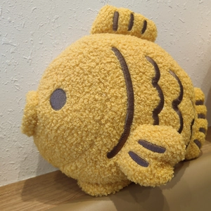 Close-up of fluffy yellow taiyaki plush pillow with detailed dark brown fish embroidery