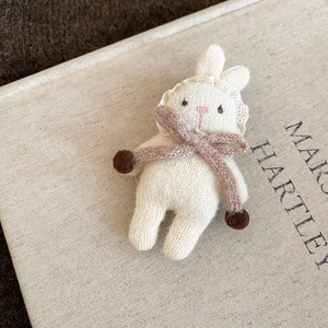 Detailed macro view of a handmade white knitted rabbit brooch with a brown scarf and lace hat
