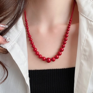 Gros plan d'un collier de perles rouges dégradées porté par un mannequin en blanc