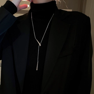 Close-up of a silver geometric teardrop pendant necklace worn over black turtleneck sweater
