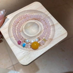 Détail de bracelets en perles de pierre rose avec perles blanches et breloque dorée