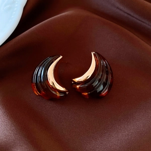 Macro shot of 18K gold crescent earrings with amber resin texture on silk background