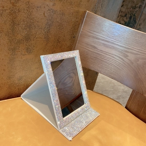 Close-up detail of silver rhinestone-studded foldable makeup mirror on a leather surface