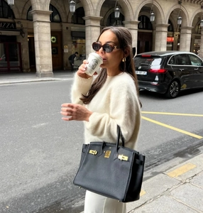 Gros plan du sac à main noir en cuir grainé avec fermoir doré porté par le mannequin
