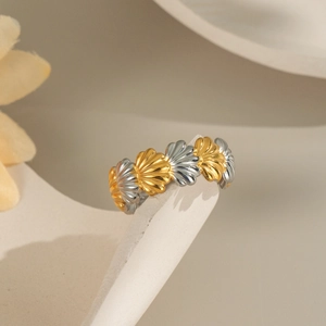 Shell-shaped gold and silver mixed metal ring displayed on an abstract geometric stand