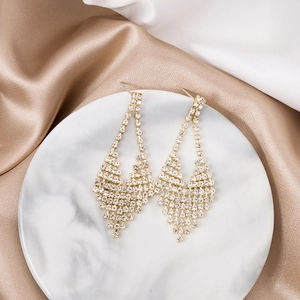 Detail of elegant gold tassel earrings with shimmering crystals on white marble and silk