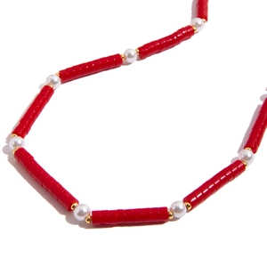 Resort style necklace with red tube beads and white pearls with gold spacers on white