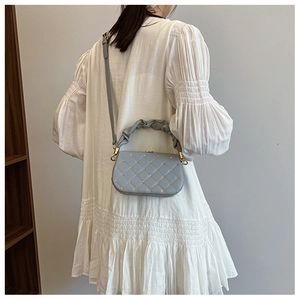 Model wearing a light blue quilted bag with gold rivets and pleated handle