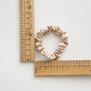Detail view of champagne satin scrunchie showing 4.5cm diameter with wood ruler measurement