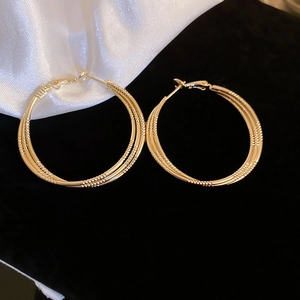 Macro detail of gold triple-hoop earrings with fine textured finish on silk backdrop