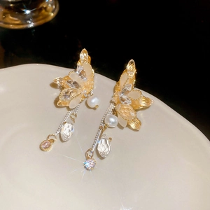 Close-up of butterfly earrings with pearls and crystals on a white ceramic plate