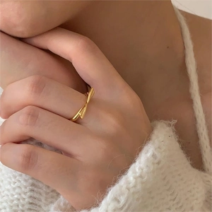 Close-up of a minimalist golden twisted knot ring worn by a model in a knit sweater