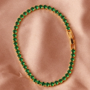 Classic emerald green zircon tennis bracelet with gold finish on pink silk backdrop