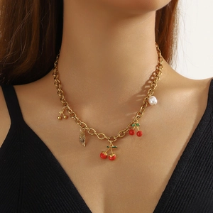 Gold chain necklace with red cherry, gold leaf and white pearl charms on a model