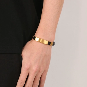 Close-up of matte gold metal plate on black braided leather bracelet for men