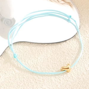 Détail macro du bracelet tressé bleu clair avec pendentif cœur doré et nœud coulissant ajustable