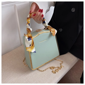 Detail of mint green box bag with textured leather, gold frame, and silk handle scarf