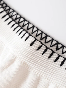 Detalle de tejido de punto blanco con costuras de contraste negras y textura