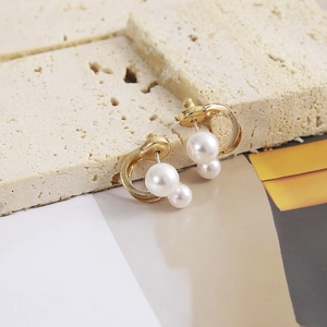 Detail showing curved gold earrings with twin white pearls on a textured stone background